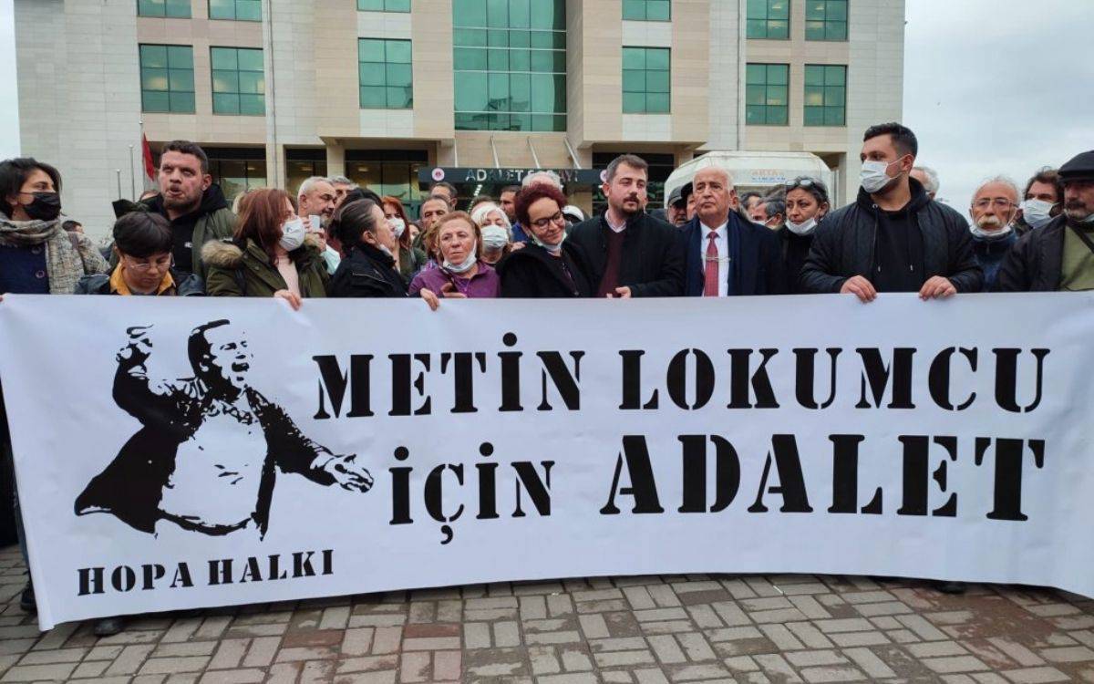 Bu fotoğrafta, bir grup insan bir pankart tutarak toplu bir şekilde protesto ediyor. Pankartta büyük harflerle "METİN LOKUMCU İÇİN ADALET" yazısı bulunuyor. Pankartın alt kısmında "HOPA HALKI" ifadesi yer almakta. Pankartın sol tarafında, Metin Lokumcu'nun öfkeli ve elini kaldırmış bir silüeti yer alıyor.