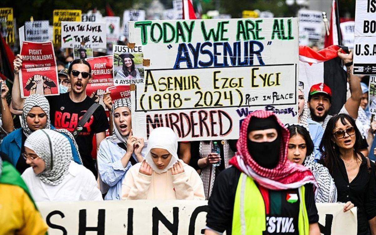 Fotoğrafta, kalabalık bir protesto veya yürüyüş sahnesi görülüyor. Ön planda çeşitli pankartlar taşıyan insanlar bulunuyor. En dikkat çeken pankartta büyük harflerle "Today we are all Ayşenur" yazıyor ve altında "Asenur Ezgi Eygi (1998-2024)" ifadesi yer alıyor. Pankart, Ayşenur'un öldürüldüğünü belirten "Murdered" kelimesiyle sona eriyor. Bu pankartın üzerinde ayrıca "Justice 4 Ayşenur" yazısı ve Ayşenur’un bir fotoğrafı yer almakta.  Katılımcılar arasında başörtülü kadınlar, gözlüklü ve siyah tişörtlü bir adam, yüzü örtülü bir kişi gibi çeşitli insanlar bulunuyor. Diğer pankartlarda "Fight Imperialism" (Emperyalizme Karşı Savaş) gibi sloganlar yer alıyor. Ayrıca, "From the river to the sea" gibi başka mesajlar içeren pankartlar da göze çarpıyor. Kalabalığın arka planında da pek çok insan, farklı pankartlar ve sloganlarla protestoya katılıyor.  Bu görüntü, bir adalet talebi ve protesto etkinliğini betimliyor. Katılımcılar, bir kişiye yönelik adaletsizliğe karşı tepkilerini dile getir