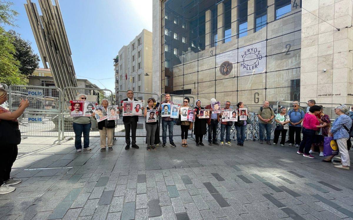 Bu fotoğrafta, bir grup insan ellerinde kayıp yakınlarının fotoğraflarını taşıyarak bir eylem gerçekleştiriyor. Fotoğrafın arka planında, büyük bir bina ve etrafında polis barikatları görülüyor. İnsanlar, üzerlerinde kayıp kişilerin adları ve fotoğraflarının bulunduğu pankartlar tutuyor. Fotoğraf, Cumartesi Anneleri'nin ya da benzeri bir grubun kayıplarının akıbetini sormak ve adalet taleplerini dile getirmek amacıyla yaptığı bir eylemi yansıtıyor gibi görünüyor. Eylemde, kayıp yakınlarının izini sürmeye devam eden kişilerin barışçıl bir şekilde toplandıkları anı gösteriyor.