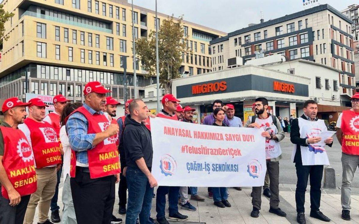 Fotoğrafta, bir grup sendika üyesi, dış mekânda toplanmış ve pankartlar taşıyor. Önde, üzerinde "Anayasal Hakkımıza Saygı Duy! #TelusİtirazıGeriÇek" yazılı büyük bir pankart bulunuyor. Pankartın alt kısmında "Çağrı-İş Sendikası" ifadesi yer alıyor. Katılımcılar arasında kırmızı yelek ve şapka giymiş kişiler dikkat çekiyor; yeleklerde "Nakliyat-İş Sendikası" yazılı. Katılımcılar, çeşitli sendikal taleplerini ifade etmek için bir araya gelmiş görünüyor.