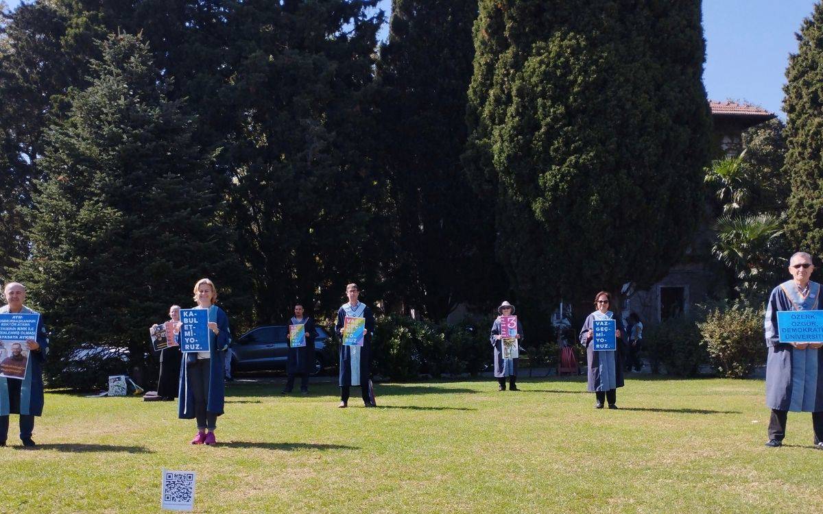 Boğaziçi Üniversitesi'nde 1377 gündür devam eden direnişin 197. haftasında, akademisyenler ve öğrenciler taleplerini dile getirmeye ve protestolarını sürdürmeye devam ediyor. Fotoğrafta, akademisyenler cübbeleriyle sosyal mesafeli bir şekilde kampüs bahçesinde duruyor ve ellerinde pankartlar taşıyorlar. Bu pankartlarda, "Kabul Etmiyoruz," "Vazgeçmiyoruz" ve "Özerk, Özgür, Demokratik Üniversite" gibi sloganlar yer alıyor.