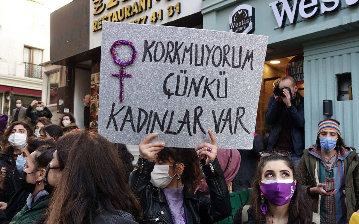 Bu fotoğraf, kadın hakları ve şiddete karşı mücadele ile ilgili bir protesto ya da etkinlik sırasında çekilmiş görünüyor. Kalabalık bir grup insan var, çoğu kadın ve birçoğu maske takmış durumda, bu da fotoğrafın pandemi döneminde çekilmiş olabileceğini düşündürüyor. Öndeki kişi, elinde parlak bir kartona yazılmış bir pankart tutuyor. Pankartta, büyük ve dikkat çekici harflerle "Korkmuyorum çünkü kadınlar var" yazıyor. Aynı pankartta, kadın sembolü de bulunuyor ve simge, parlak mor ya da pembe süslemelerle vurgulanmış.  Arka planda, etkinliği fotoğraflayan başka bir kişi de göze çarpıyor. Genel olarak, bu görüntü, kadın dayanışması ve şiddete karşı duruşu ifade eden bir protestoyu yansıtıyor.