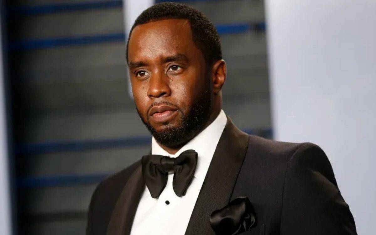 otoğrafta, Amerikalı rapçi ve yapımcı Sean Combs, bilinen adıyla "Diddy", resmi bir ortamda görülüyor. Diddy, siyah bir smokin giymiş, beyaz gömlek ve siyah bir papyon takıyor. Yüz ifadesi ciddi ve düşünceli, gözleri bir noktaya odaklanmış. Arka plan bulanık, odak tamamen Diddy'nin üzerinde. Genel olarak fotoğraf, ciddi ve resmi bir atmosferi yansıtıyor.