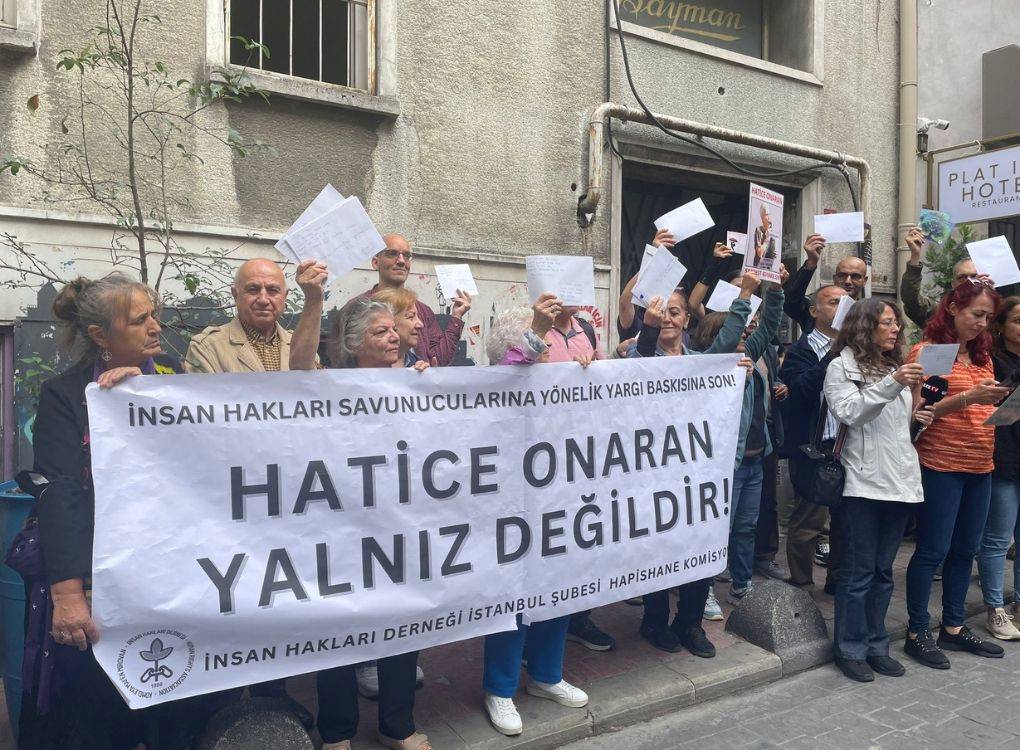 Fotoğrafta, İnsan Hakları Derneği İstanbul Şubesi Hapishane Komisyonu üyelerinden oluşan bir grup insan, Hatice Onaran'a destek amaçlı bir eylem gerçekleştiriyor. Katılımcılar, ellerinde zarflar ve mektuplar tutarak dayanışma mesajları veriyorlar. Grup, büyük bir pankart açmış; pankartta "İnsan Hakları Savunucularına Yönelik Yargı Baskısına Son! Hatice Onaran Yalnız Değildir!" yazıyor.