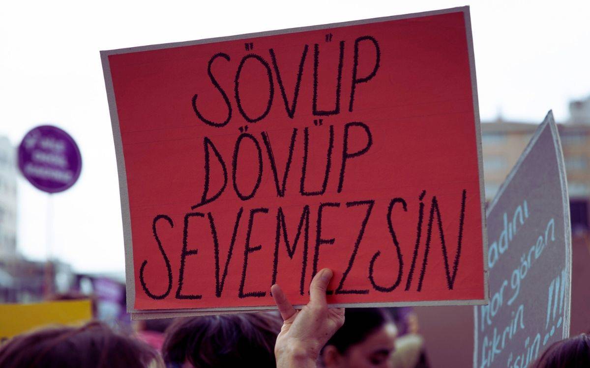 Bu görselde, bir protesto veya eylem sırasında taşınan bir pankart görülüyor. Pankart kırmızı bir zemin üzerine siyah el yazısıyla yazılmış büyük harflerle şu ifadeyi içeriyor: "Sövüp dövüp sevemezsin."  Bu güçlü mesaj, kadınlara yönelik şiddeti ve kötü muameleyi kınayan bir uyarı niteliğinde. İfade, hem sözlü hem de fiziksel şiddetin sevgiyle bağdaşamayacağını vurguluyor. Arka planda belirsiz başka pankartlar da görünüyor, ancak ana odak bu kırmızı pankart üzerinde. Protestonun amacı muhtemelen toplumsal cinsiyet eşitliği, kadın hakları ve kadına yönelik şiddetle mücadele gibi konularla ilgili.