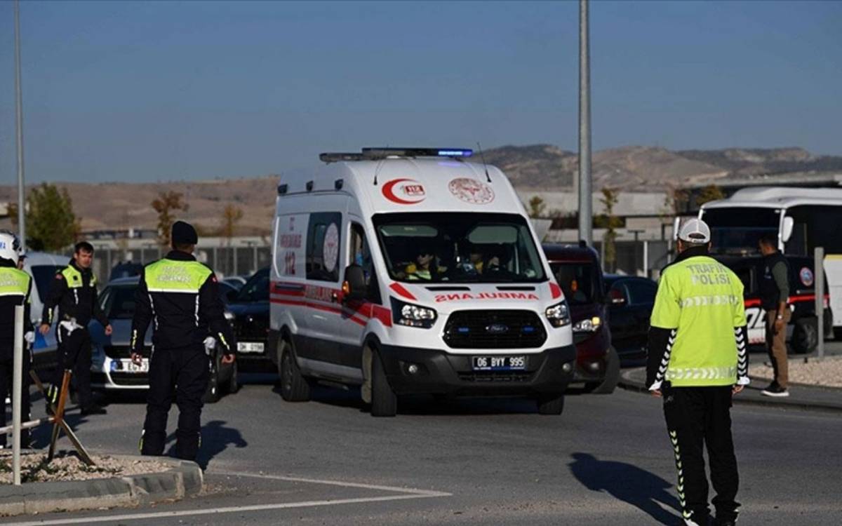 Bu fotoğrafta bir ambulansın bulunduğu bir trafik denetimi sahnesi yer alıyor. Ambulans, ön kısmında "112 Acil" yazısıyla görülüyor ve sağ şeritte hareket ediyor. Çevresinde birkaç trafik polisi var; çoğu sarı yelek giymiş ve durumu yönetiyor gibi görünüyor. Arka planda, açık bir alan ve tepelerle çevrili bir manzara bulunuyor. Fotoğraf büyük olasılıkla açık bir havada, gün ortasında çekilmiş.