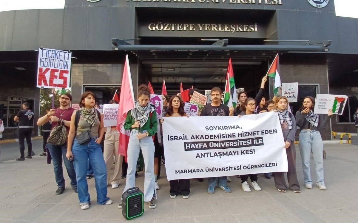 Görselde, Marmara Üniversitesi'nin Göztepe Yerleşkesi önünde toplanmış bir grup öğrenci, İsrail ve Haifa Üniversitesi ile yapılan akademik anlaşmalara karşı bir protesto düzenliyor. Öğrenciler, büyük bir pankart tutarak üzerinde “Soykırıma, İsrail akademisine hizmet eden Haifa Üniversitesi ile anlaşmayı kes! Marmara Üniversitesi Öğrencileri” yazısını taşıyor.