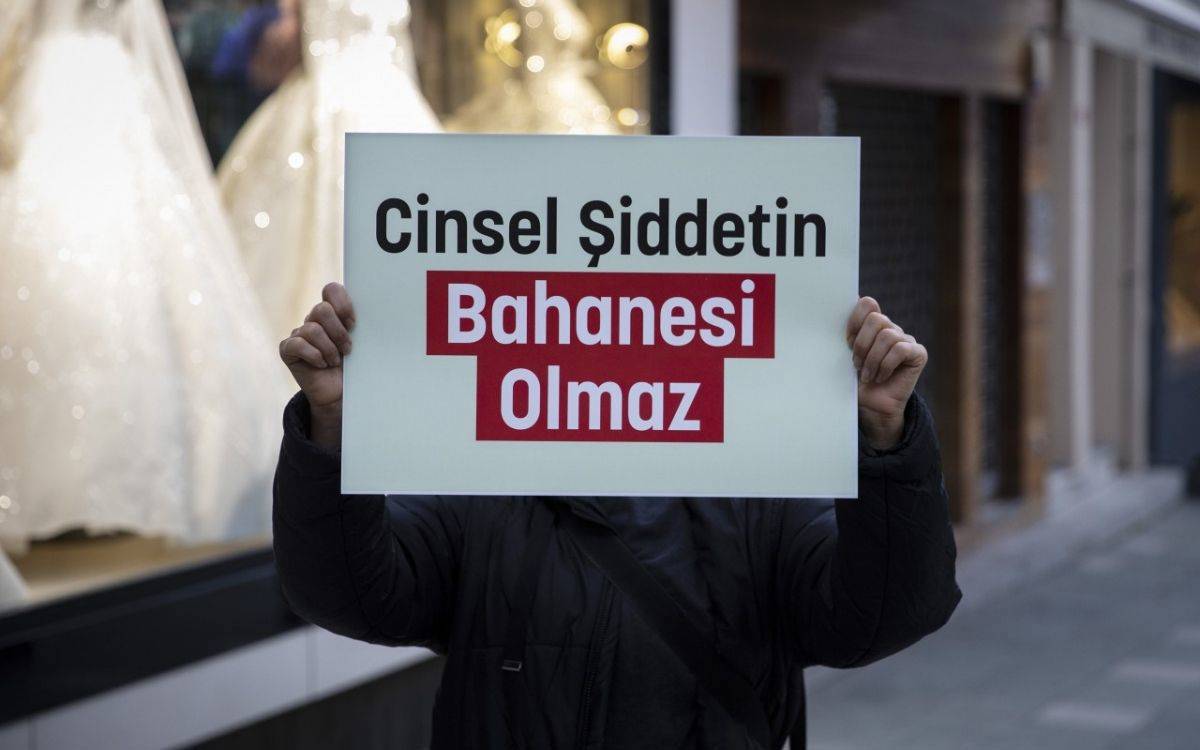 Fotoğrafta, bir protesto veya farkındalık etkinliğinde tutulan bir pankart dikkat çekiyor. Beyaz zemin üzerine yazılmış pankartta, "Cinsel Şiddetin Bahane­si Olmaz" yazısı yer alıyor. "Bahane­si Olmaz" ifadesi kırmızı bir kutunun içinde beyaz harflerle vurgulanmış. Pankartı tutan kişinin yüzü görünmüyor, yalnızca elleri ve montu görülüyor. Arka planda gelinliklerin sergilendiği bir mağaza vitrini seçilebiliyor. Bu mesaj, cinsel şiddete karşı sıfır tolerans ve mazeret kabul etmeme çağrısını ifade ediyor.