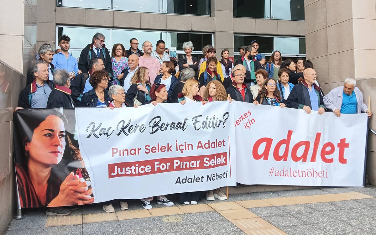 Fotoğrafta, Pınar Selek'e destek için bir grup insan, bir binanın önünde toplanmış durumda. Önde, büyük bir pankart taşınıyor. Pankartta, "Kaç Kere Beraat Edilir? Pınar Selek İçin Adalet / Justice For Pinar Selek" ve "Adalet Nöbeti" yazıları dikkat çekiyor. Aynı zamanda "Herkes İçin Adalet" ifadesi ve "#adaletnöbeti" etiketi de pankartta yer alıyor.  Katılımcılar arasında farklı yaşlardan insanlar bulunuyor ve çoğu, dayanışma duygusuyla pankartların arkasında yer alıyor. Bazı kişilerin elleri pankartlarda, diğerleri ise çevrede dayanışma halinde bekliyor. Topluluk, Pınar Selek davasında yaşanan adaletsizliklere dikkat çekmek amacıyla bir araya gelmiş, kararlı ve dayanışmacı bir görüntü sergiliyor.