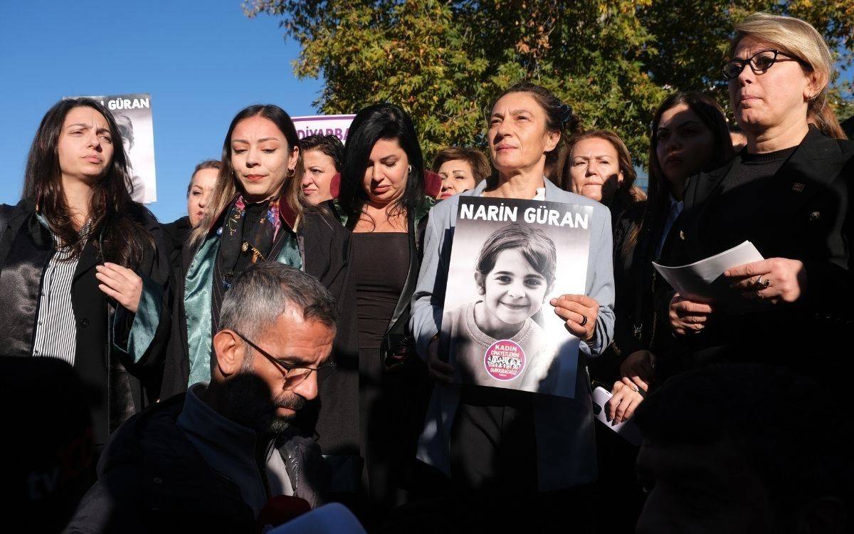 Fotoğrafta, bir grup kadın dışarıda bir araya gelmiş, arka planda ağaçlar ve gökyüzü görülüyor. Ortada, elinde genç bir kız çocuğunun siyah beyaz fotoğrafını taşıyan bir kadın dikkat çekiyor. Fotoğrafta “Narin Güran” yazısı ve çocuğun yüzünde gülümseme var. Poster üzerinde “Kadın cinayetlerini durduracağız” yazan bir sticker mevcut. Kadınların çoğu ciddi ve kararlı ifadelerle fotoğrafa bakıyorlar; birçoğu siyah kıyafetler ve cübbe giymiş.  Bu topluluk muhtemelen bir anma ya da kadın haklarıyla ilgili bir farkındalık etkinliğine katılıyor.