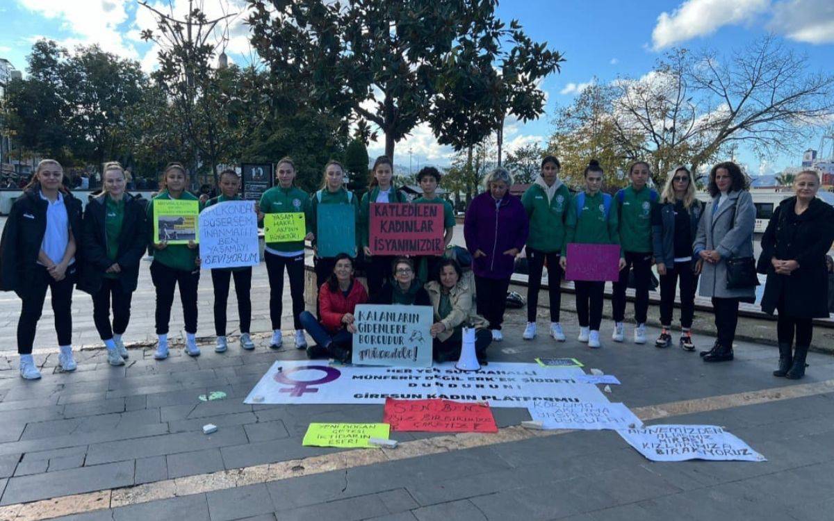 Bu fotoğraf, açık bir alanda, özellikle bir meydanda, bir grup kadının dayanışma gösterisini betimliyor. Giresun Kadın Platformu’nun düzenlediği "Yaşam Nöbeti" etkinliğine katılan Giresun Sanayispor Kadın Futbol Takımı oyuncuları, çeşitli pankartlar ve dövizler taşıyarak etkinliğe destek veriyorlar.