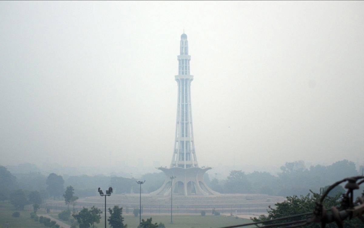 Fotoğrafta Pakistan’ın başkenti Lahor’da bulunan ve şehrin simgelerinden biri olan Minar-e-Pakistan anıtı yer almaktadır. Anıtın çevresi yoğun bir sis veya hava kirliliği tabakasıyla kaplanmış durumdadır, bu da görüş mesafesini ciddi şekilde kısıtlamaktadır. Hava kirliliği nedeniyle anıtın çevresindeki ağaçlar ve diğer yapılar soluk bir şekilde görünmektedir. Görselde genel olarak gri tonlar hakim olup, kirlilik nedeniyle anıtın net bir şekilde görülemediği dikkat çekmektedir. Bu durum, bölgedeki ciddi hava kirliliği sorununa işaret etmektedir.