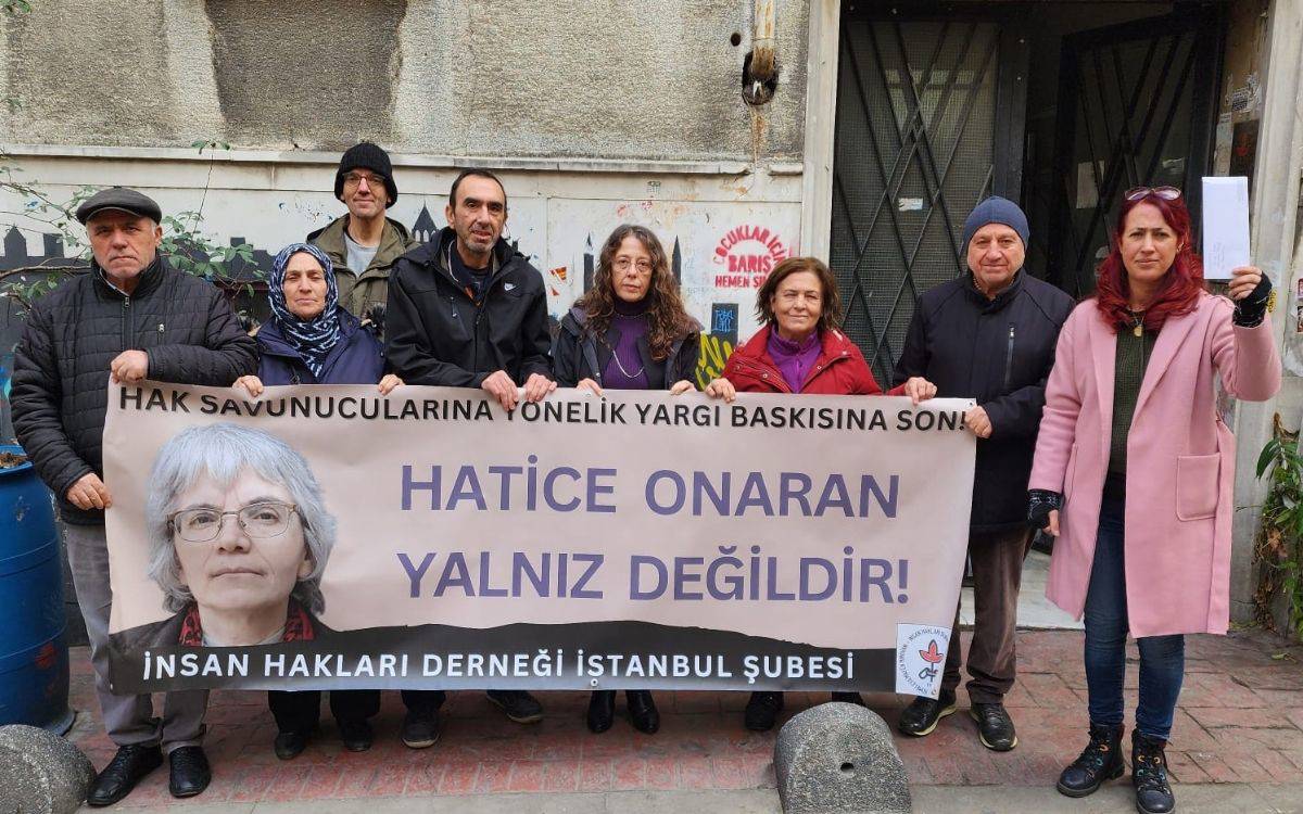 Fotoğrafta, bir grup insan açık bir alanda bir araya gelmiş ve bir pankart tutuyor. Pankartta büyük harflerle "Hak Savunucularına Yönelik Yargı Baskısına Son! Hatice Onaran Yalnız Değildir!" yazısı yer alıyor. Ayrıca, pankartın sol tarafında Hatice Onaran'ın bir fotoğrafı bulunuyor. Alt kısımda ise "İnsan Hakları Derneği İstanbul Şubesi" ifadesi görülüyor.  Grup üyeleri çeşitli yaşlarda ve farklı kıyafetlerle dikkat çekiyor. Arka planda eski bir bina ve kapılar bulunuyor. Fotoğraf, insan hakları savunucuları ve sivil toplum aktivistlerinin, Hatice Onaran’a desteklerini göstermek için düzenledikleri bir dayanışma etkinliğini yansıtıyor. Sağdaki bir kadın elinde bir zarf tutarak dikkat çekiyor, bu da sembolik bir mesaj ya da belge olabilir.