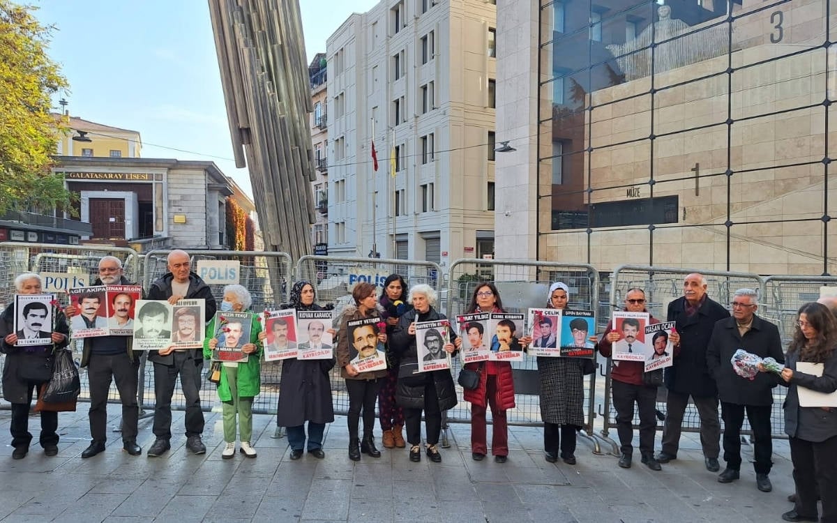 Cumartesi Anneler/İnsanları 1027. Hafta buluşmasında Galatasaray Meydanı'nda bariyerlerin önünde. Ellerinde gözaltında kaybedilenlerin fotoğrafları ve karanfiller var.