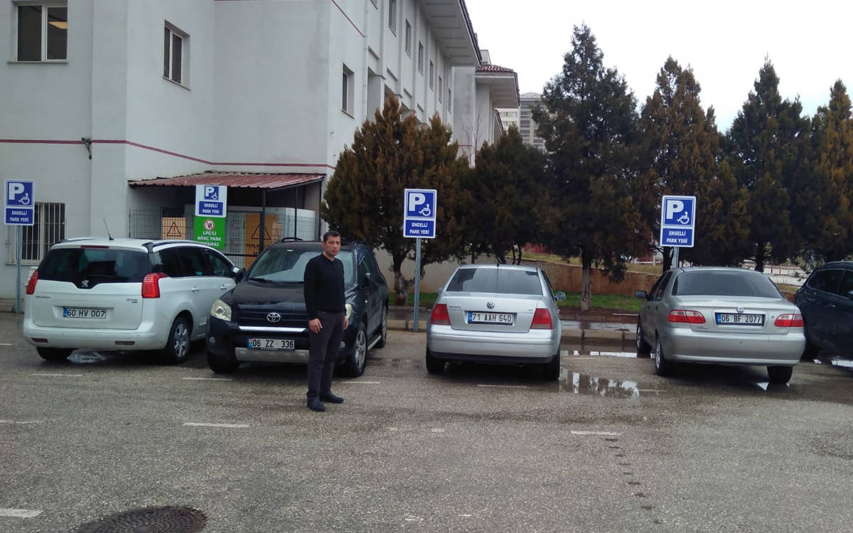 Engelli park yerini işgal eden araçlar. Bir kişi dört aracın önünde kameraya bakarak poz veriyor.