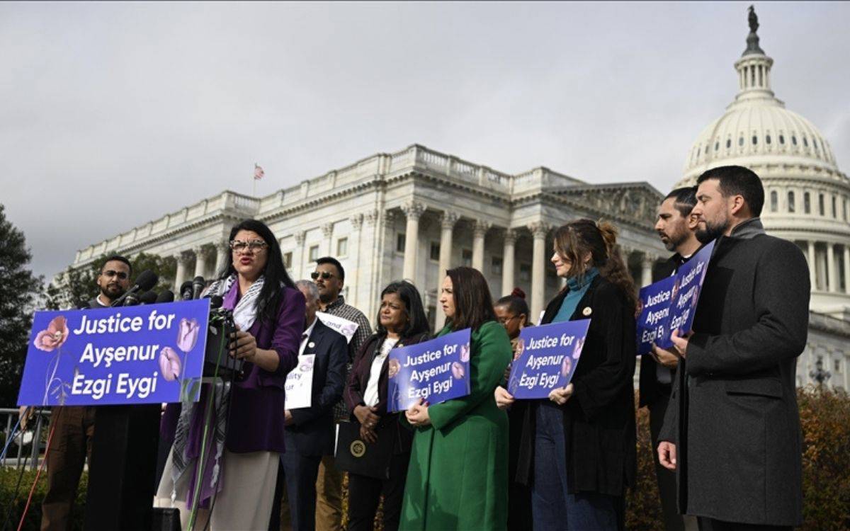 Bu görselde, Amerika Birleşik Devletleri Kongre Binası'nın (Capitol Hill) önünde düzenlenen bir basın açıklaması veya protesto etkinliği görülmektedir. Görselde birkaç kişi ellerinde pankartlar taşımakta ve konuşmacı kürsüden konuşma yapmaktadır. Pankartların üzerinde "Justice for Ayşenur Ezgi Eygi" (Ayşenur Ezgi Eygi için Adalet) yazmaktadır ve tasarımda çiçek desenleri kullanılmıştır.