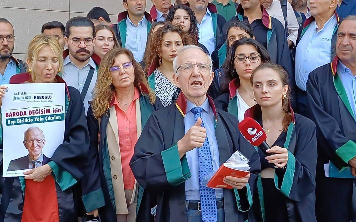 Fotoğrafta, avukat cübbeleri giymiş bir grup insan toplu halde poz vermektedir. Ön planda, elinde bir mikrofon ve kitap tutan bir erkek konuşma yaparken görülüyor. Yanında ve arkasında yer alan diğer avukatlar ciddi bir şekilde konuşmayı dinlemektedir. Sol tarafta bir kişi, üzerinde “Baroda Değişim İçin Hep Birlikte Yola Çıkalım” yazılı bir afiş tutmaktadır. Afişte bir kişinin fotoğrafı ve ismi yer almaktadır. Grup, toplumsal veya mesleki bir konuda dayanışma ve değişim mesajı vermek için bir araya gelmiş gibi görünmektedir. Arkada topluluk yoğunluğu ve çeşitli yüz ifadeleri dikkat çekiyor.