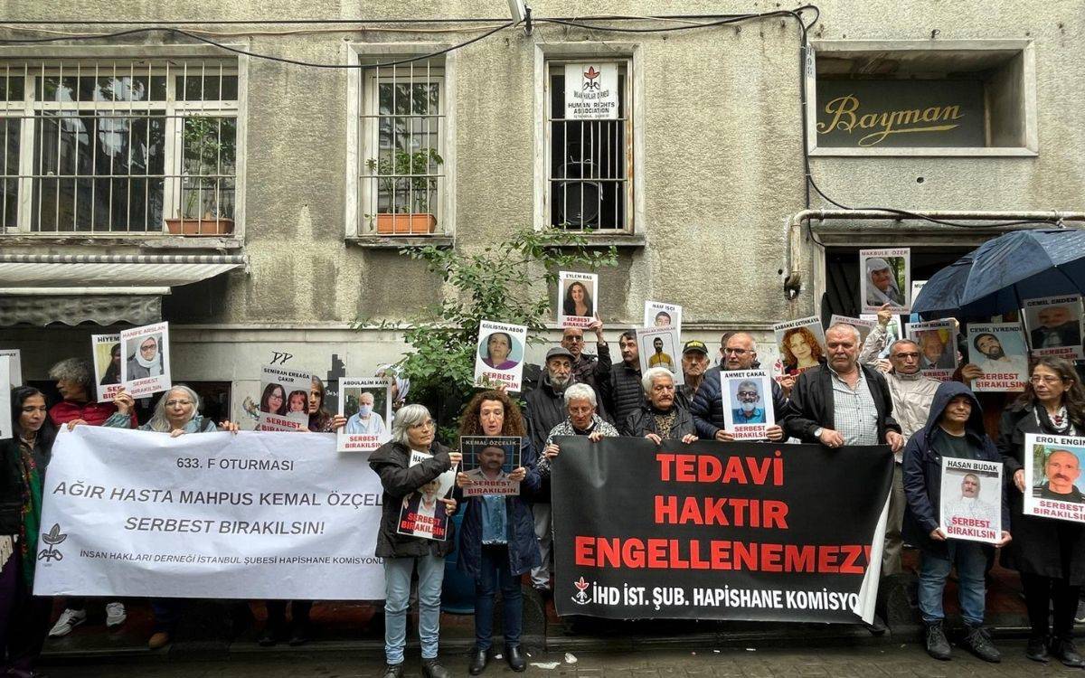 Fotoğrafta, bir grup insan İnsan Hakları Derneği'nin düzenlediği bir etkinlikte bir araya gelmiş durumda. Arka planda eski bir bina görünmekte, binanın pencerelerinde saksılar yer alıyor. Etkinlikte, ellerinde pankartlar ve hasta mahpusların serbest bırakılmasını talep eden dövizler tutan insanlar var.  Büyük bir pankartta "633. F Oturması, Ağır Hasta Mahpus Kemal Özçelik Serbest Bırakılsın! İnsan Hakları Derneği İstanbul Şubesi Hapishane Komisyonu" yazısı yer alıyor. Bir diğer pankartta ise "Tedavi Haktır, Engellenemez" ifadesi dikkat çekiyor. Katılımcılar, ellerinde hasta mahpusların fotoğraflarını tutarak desteklerini ifade ediyorlar. Hava bulutlu görünüyor, bazı kişiler şemsiye kullanmış. Protesto, hasta mahpusların sağlık ve yaşam haklarına dikkat çekmek ve serbest bırakılmalarını talep etmek amacıyla düzenlenmiş bir etkinlik olarak görünüyor.