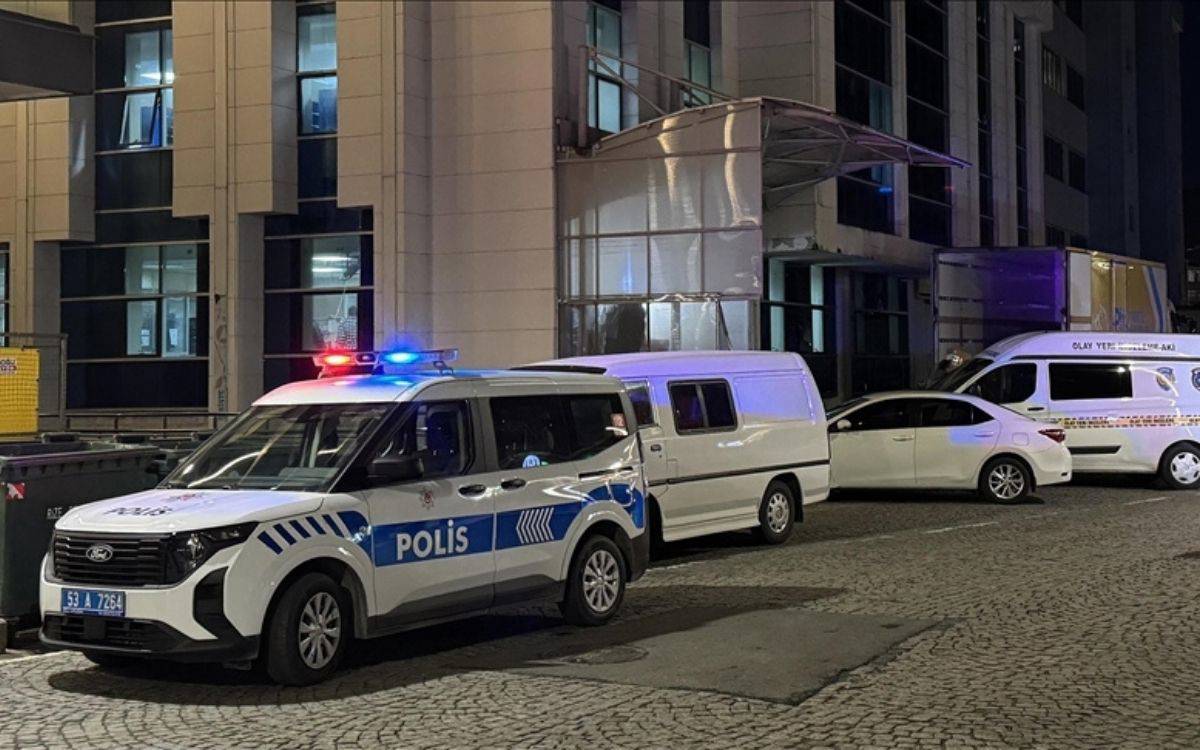 Bu görsel, bir olay yerinde çekilmiş gibi görünüyor. Görüntüde birkaç polis aracı ve bir olay yeri inceleme aracı dikkat çekiyor. Polis araçlarının üzerinde mavi ve kırmızı siren lambaları yanmakta, bu da olay yerinde aktif bir incelemenin sürdüğünü gösteriyor.  Arka planda modern bir bina yer alıyor, bu bina muhtemelen bir iş yeri veya kamu kurumu olabilir. Araçların konumu, olay yerinin bina çevresinde yoğunlaştığını düşündürüyor. Yerde parke taşlarıyla döşeli bir yol var ve araçlar düzgün bir şekilde park edilmiş gibi görünüyor. Genel olarak, olay yerindeki ekiplerin inceleme ve güvenlik önlemleri için çalıştığı bir sahne yansıtılmış.