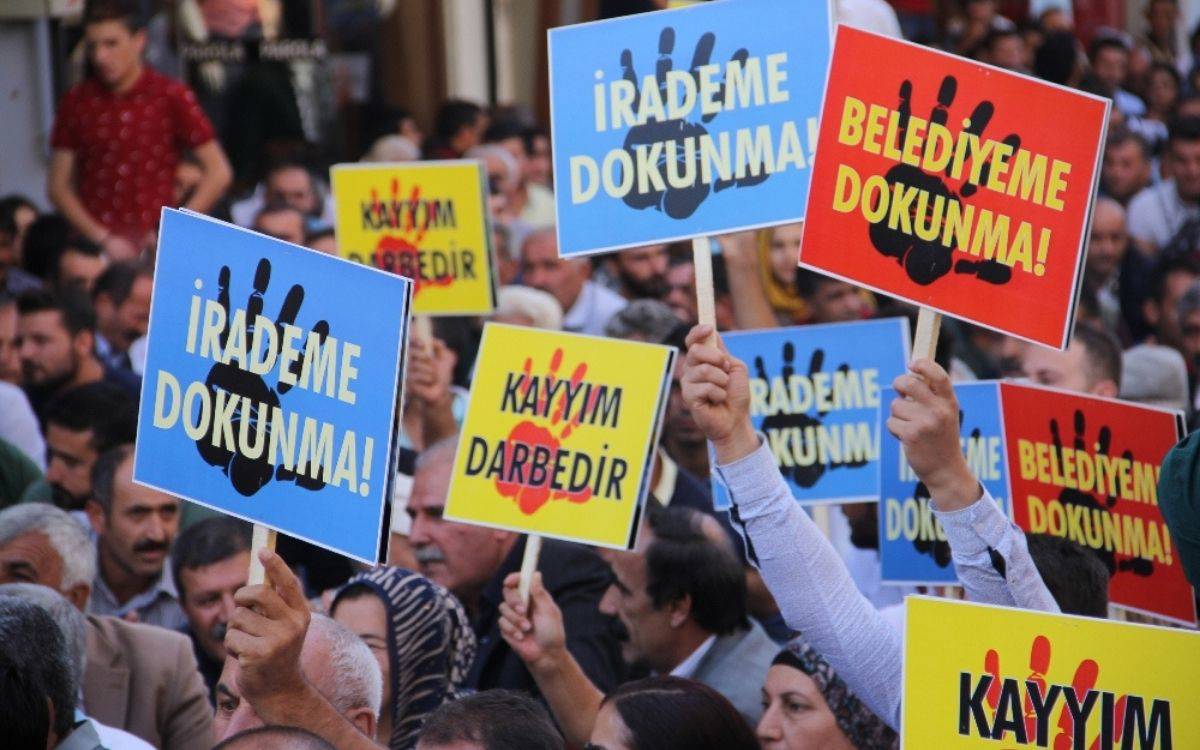 Fotoğrafta, kayyım atamalarını protesto eden bir grup görünüyor. Eyleme katılanlar ellerinde, "Belediyeme dokunma", "kayyım darbedir" pankartı taşıyor.