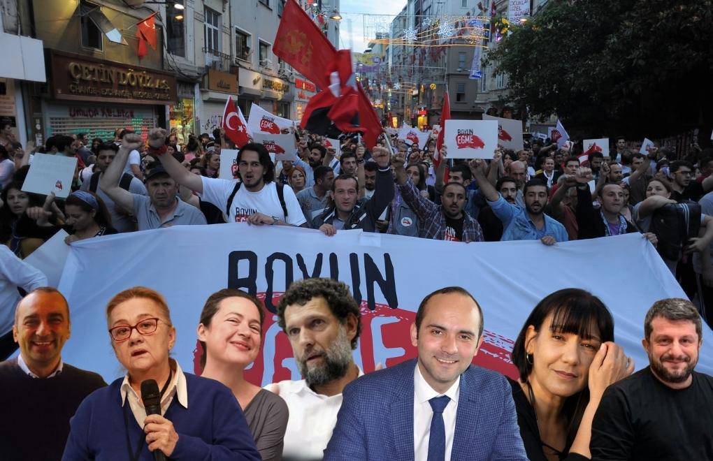 Bu görselde, bir protesto veya yürüyüş sırasında çekilmiş bir an görülmektedir. Arka planda, ellerinde pankartlar ve bayraklar taşıyan kalabalık bir grup yürüyüşe katılmıştır. Kalabalık, üzerinde "Boyun Eğme" yazılı büyük bir pankart taşımaktadır. Çevrede çeşitli Türkiye bayrakları ve farklı afişler de dikkat çekmektedir. Kalabalığın genel atmosferi kararlı ve protesto ruhunu yansıtır niteliktedir.  Ön planda ise Gezi Davası ile ilişkilendirilen bazı tanınmış kişiler bir montaj şeklinde eklenmiş. Bu kişilerden biri Osman Kavala olup, onun yanında Mücella Yapıcı ve diğer aktivistler yer almaktadır. Görsel, protesto ve dayanışma mesajını güçlü bir şekilde aktarmakta ve toplumsal bir mücadeleyi simgelemektedir