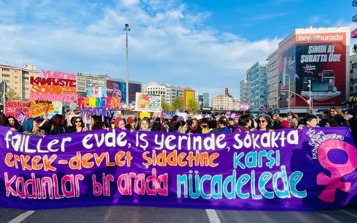 Bu fotoğraf, kadınların erkek ve devlet şiddetine karşı sokakta, birlikte mücadele ettikleri bir eylemi betimliyor. Kalabalık bir kadın grubu, büyük bir pankart taşıyarak yürüyüş düzenliyor.