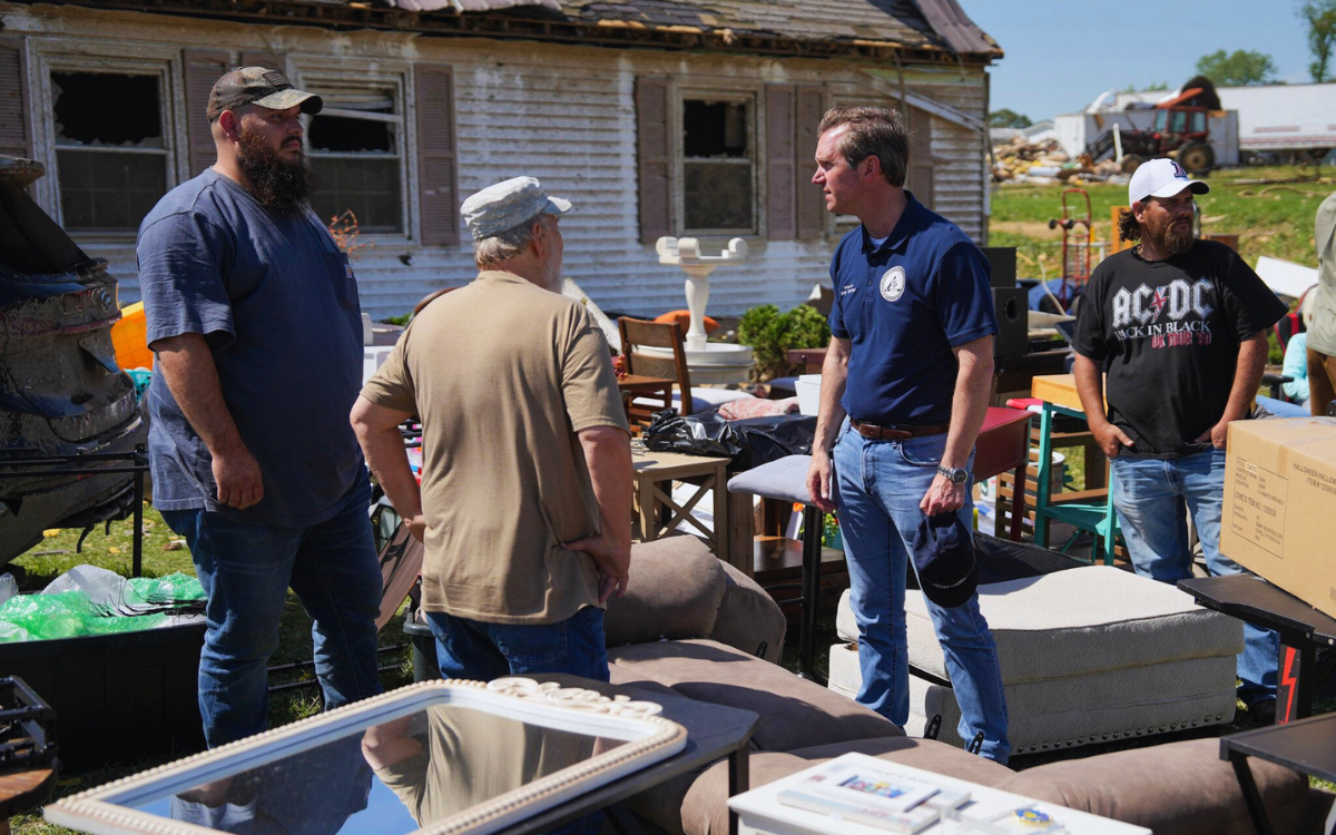 Fotoğrafta kasırgadan etkilenen kişiler ile vali konuşuyor. Etrafta dağılmış eşyalar var.