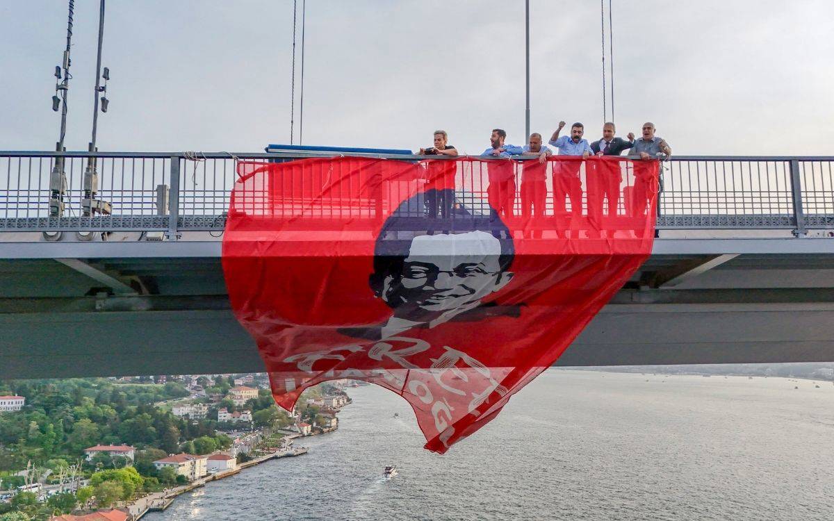 Fotoğrafta, İstanbul’daki 15 Temmuz Şehitler Köprüsü (eski adıyla Boğaziçi Köprüsü) üzerinde eylem yapan bir grup kişi görülüyor. Köprünün demir korkuluklarının arkasında, aralarında CHP milletvekillerinin de bulunduğu altı kişi yer alıyor. Grup, büyük boyutlu kırmızı bir pankart açmış. Pankartta Ekrem İmamoğlu'nun yüzü stilize bir şekilde yer alıyor ve üzerinde beyaz harflerle "FREE İMAMOĞLU" ifadesi okunuyor.