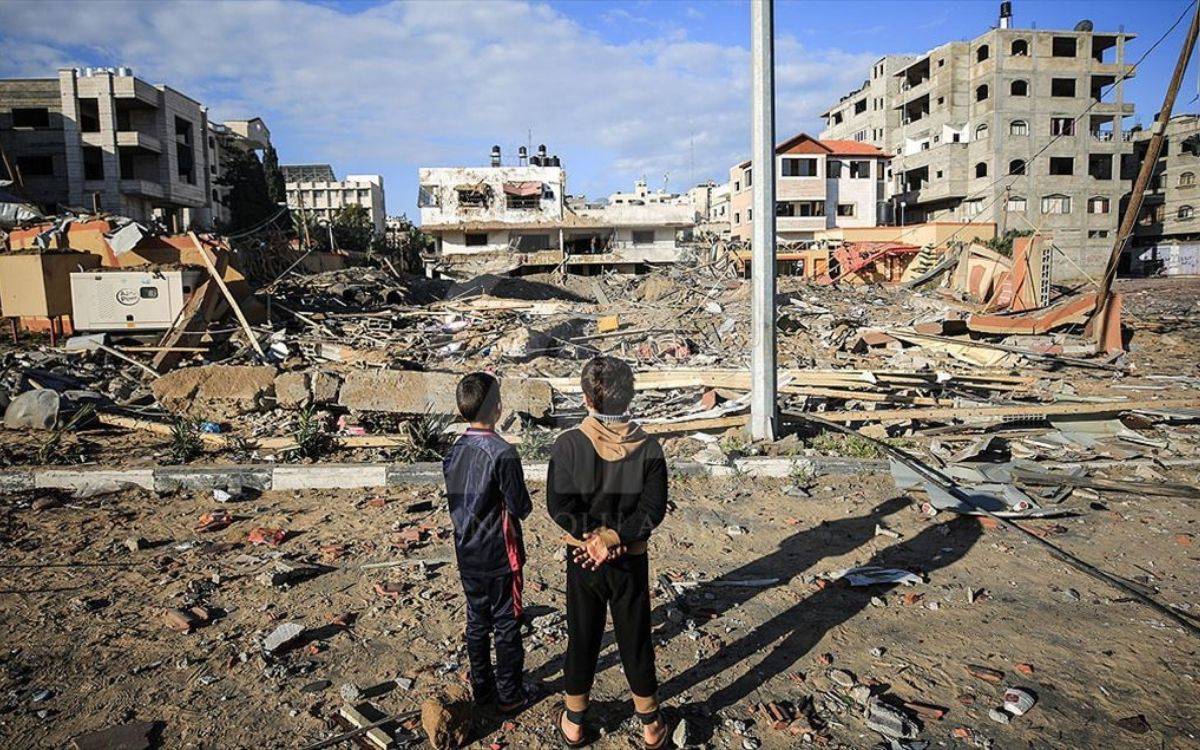 Fotoğrafta, iki çocuk yıkıntılarla dolu bir alanın önünde duruyor ve arkaları dönük şekilde manzarayı izliyor. Önlerinde tamamen yıkılmış binalar, moloz yığınları, devrilmiş direkler ve enkaza karışmış eşyalar yer alıyor. Arka planda hasar görmüş çok katlı binalar hâlâ ayakta duruyor ancak cepheleri ağır hasarlı. Gökyüzü parçalı bulutlu ve gündüz vakti olduğu anlaşılıyor.