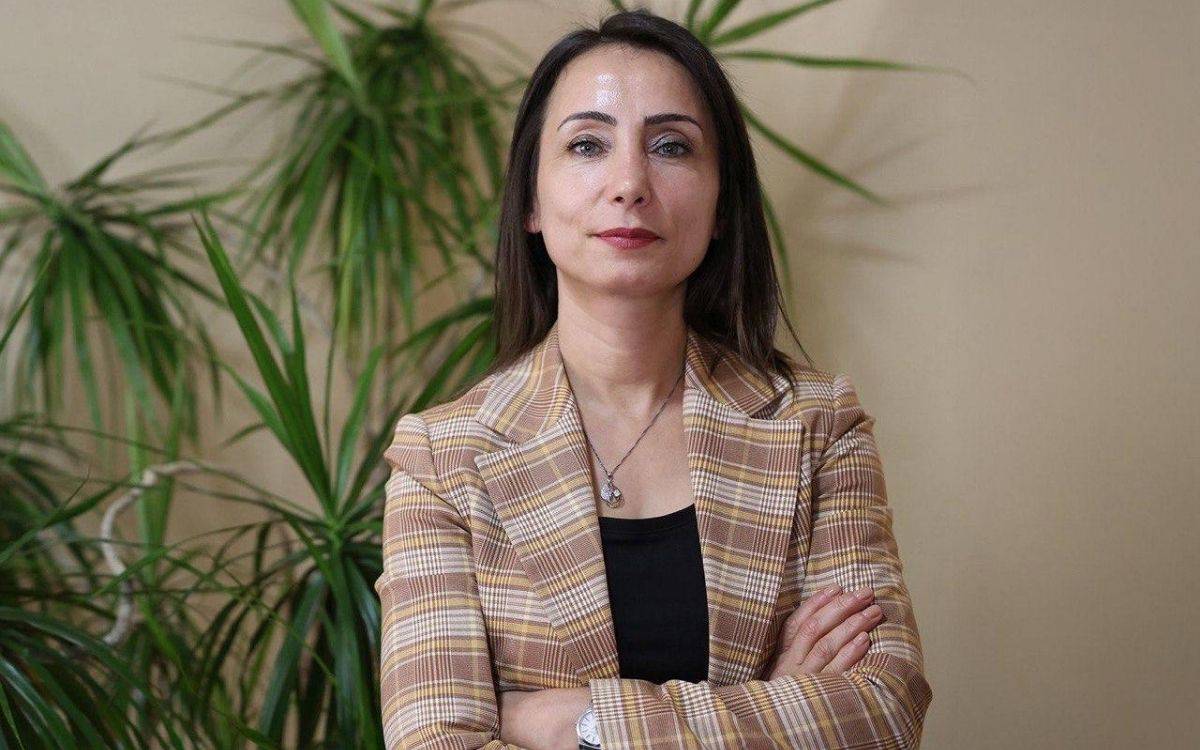 Fotoğrafta bir kadın nötr bir arka plan önünde, kollarını göğsünde kavuşturmuş şekilde kameraya bakıyor. (Yapay zeka ile üretildi)