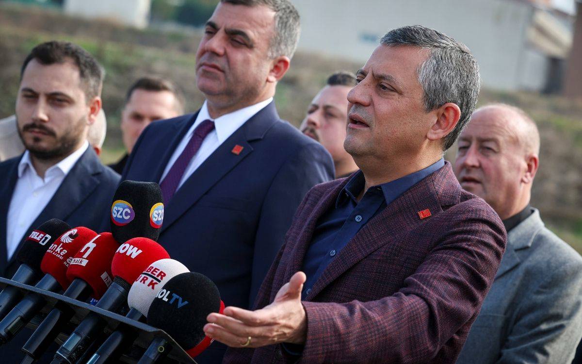 Fotoğrafta bir grup erkek dış mekânda, basın açıklaması sırasında görülüyor. Ön planda, takım elbise giymiş birkaç kişi ile birlikte, elini açık bir jestle uzatarak konuşan bir adam yer alıyor.