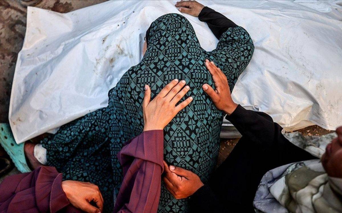 Fotoğrafta yerde beyaz bir örtüyle kaplanmış bir beden görülüyor. Örtünün yanında oturan bir kadın, başını örtüye doğru eğmiş; yeşil ve siyah desenli bir elbise giymiş. Kadının sırtına ve omzuna, çevresindekiler destek verircesine ellerini koymuş. Sahne büyük bir acı, yas ve dayanışma anını yansıtıyor. Ortam sade ve duygusal bir atmosfer taşıyor; fotoğraf kayıp, keder ve insanî dayanışmayı güçlü bir biçimde hissettiriyor.