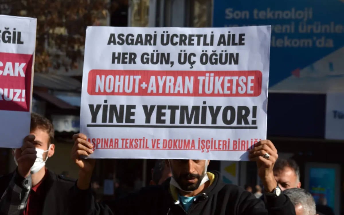 Fotoğrafta "Asgari ücretli aile her gün, üç öğün nohut pilav tüketse yine de yetmiyor" dövizi tutan bir işçi yer alıyor.