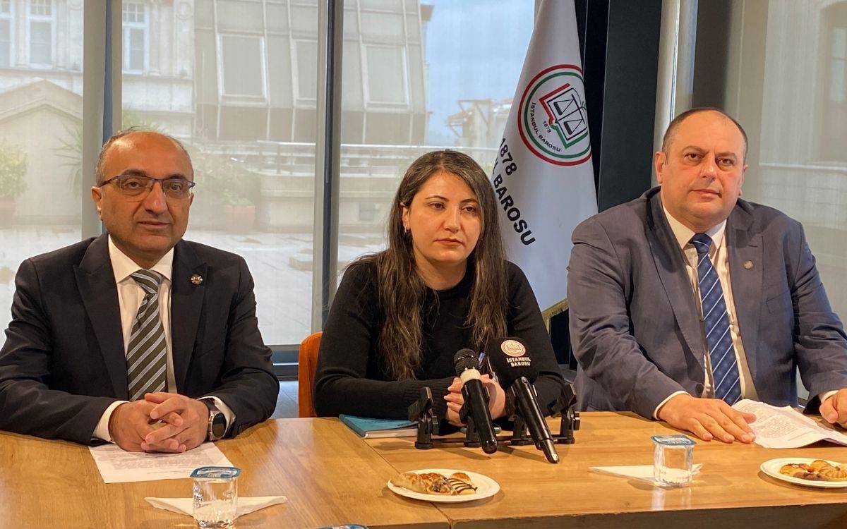 Fotoğrafta bir basın açıklaması ya da toplantı anı görülüyor. Ahşap bir masanın arkasında yan yana oturan üç kişi var. Ortada koyu renk kıyafetli bir kadın, iki yanında ise takım elbiseli iki erkek bulunuyor. Masanın üzerinde mikrofonlar, kâğıtlar, su bardakları ve küçük tabaklarda atıştırmalıklar yer alıyor.  Arka planda büyük camlar ve iç mekânın dışa bakan cephesi görülüyor. Sağ tarafta ise üzerinde “İstanbul Barosu” amblemi bulunan bir bayrak dikkat çekiyor. Genel atmosfer resmi ve ciddi; katılımcıların yüz ifadeleri de açıklama ya da duyuru yapılan bir toplantı havasını yansıtıyor.