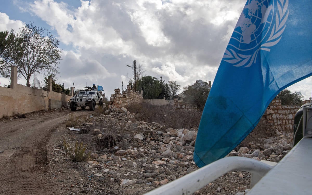 Fotoğrafta devriye atan silahlı UNIFIL aracı gözüküyor. Araç beyaz renkte ve BM bayrağı taşıyor. Yıkılmış bahçe duvarı kalıntılarının arasındaki bir sokaktan ilerliyor.