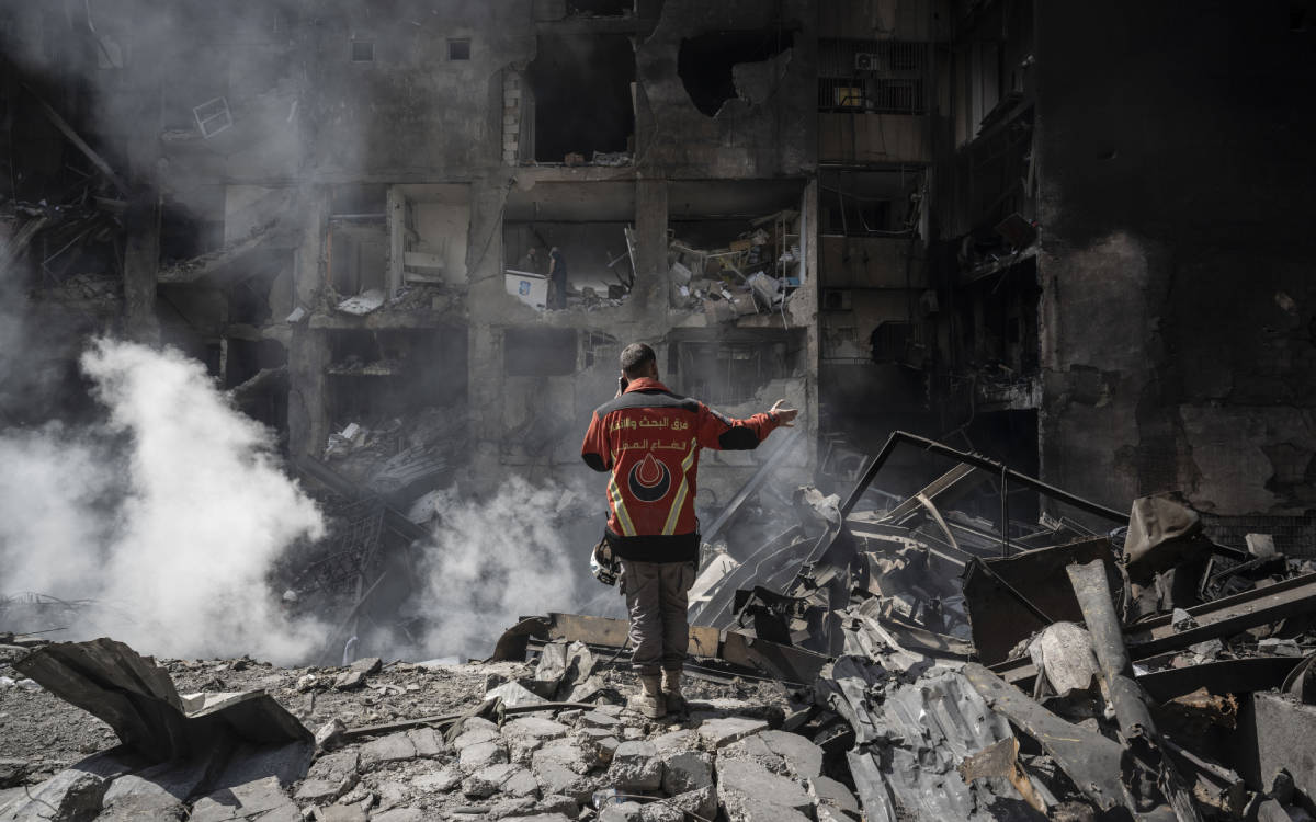 Fotoğraf İsrail'in Lübnan'da en büyük saldırılarını gerçekleştirdiği 8 Nisan'dan. Bir ilk yardım görevlisi bombalanan binaların arasında telefonla konuşuyor. Duvarları yıkılmış evlerin içlerindeki insanlar gözüküyor.