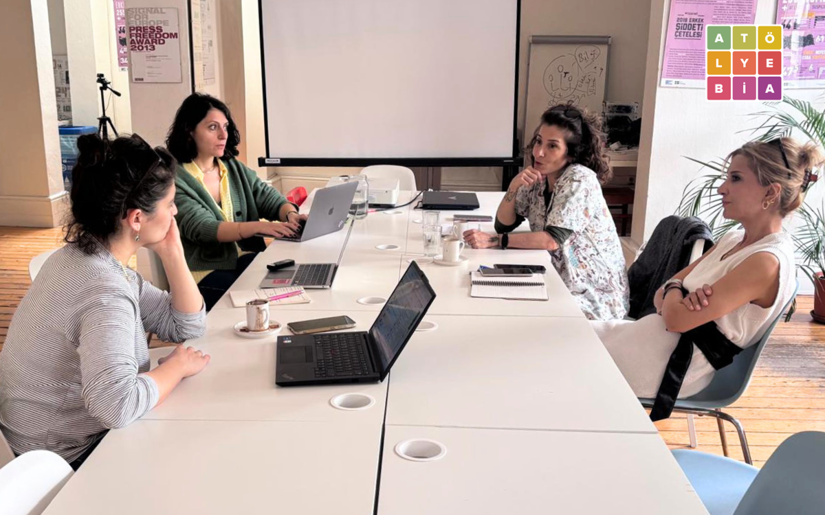 Atölye BİA’da düzenlenen görüşmede, katılımcılar uzun bir masa etrafında oturarak karşılıklı değerlendirmelerde bulunuyor. Toplantı odasında dizüstü bilgisayarlar, not defterleri ve projeksiyon perdesi dikkat çekerken, samimi ve odaklı bir çalışma ortamı öne çıkıyor.