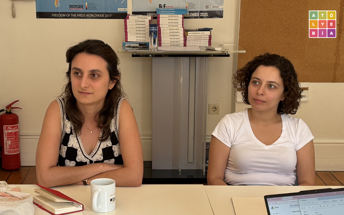 İki kişi, Atölye BİA ofisinde düzenlenen toplantıda yan yana oturarak konuşmaları dinliyor. Önlerinde not defterleri, bir dizüstü bilgisayar ve bir kahve kupası bulunuyor. Arka planda Reporters Without Borders (RSF) afişleri, raf üzerinde kitaplar ve Atölye BİA logosu yer alıyor. Toplantı ortamı sade ve resmi olmayan bir çalışma atmosferi yansıtıyor.