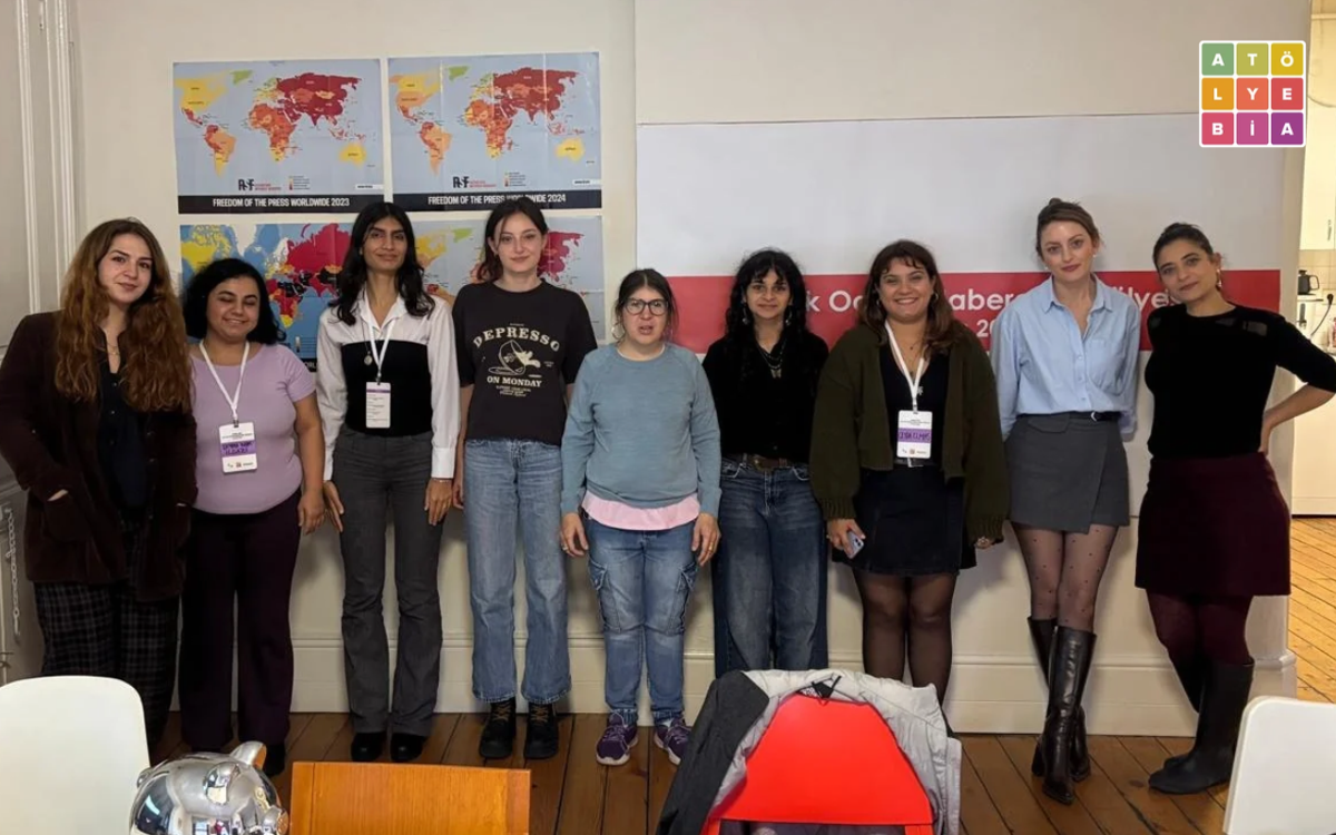 Atölye BİA’nın ofisinde, duvardaki haritalar ve atölye afişinin önünde yan yana duran dokuz kişi kameraya poz veriyor.