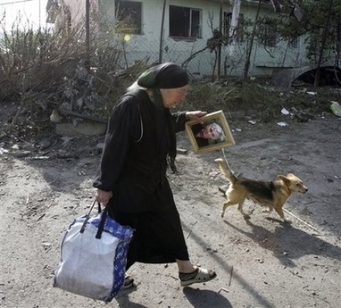 Gori'de bir kadın eşyaları ve eşinin fotoğrafıyla yürüyor.