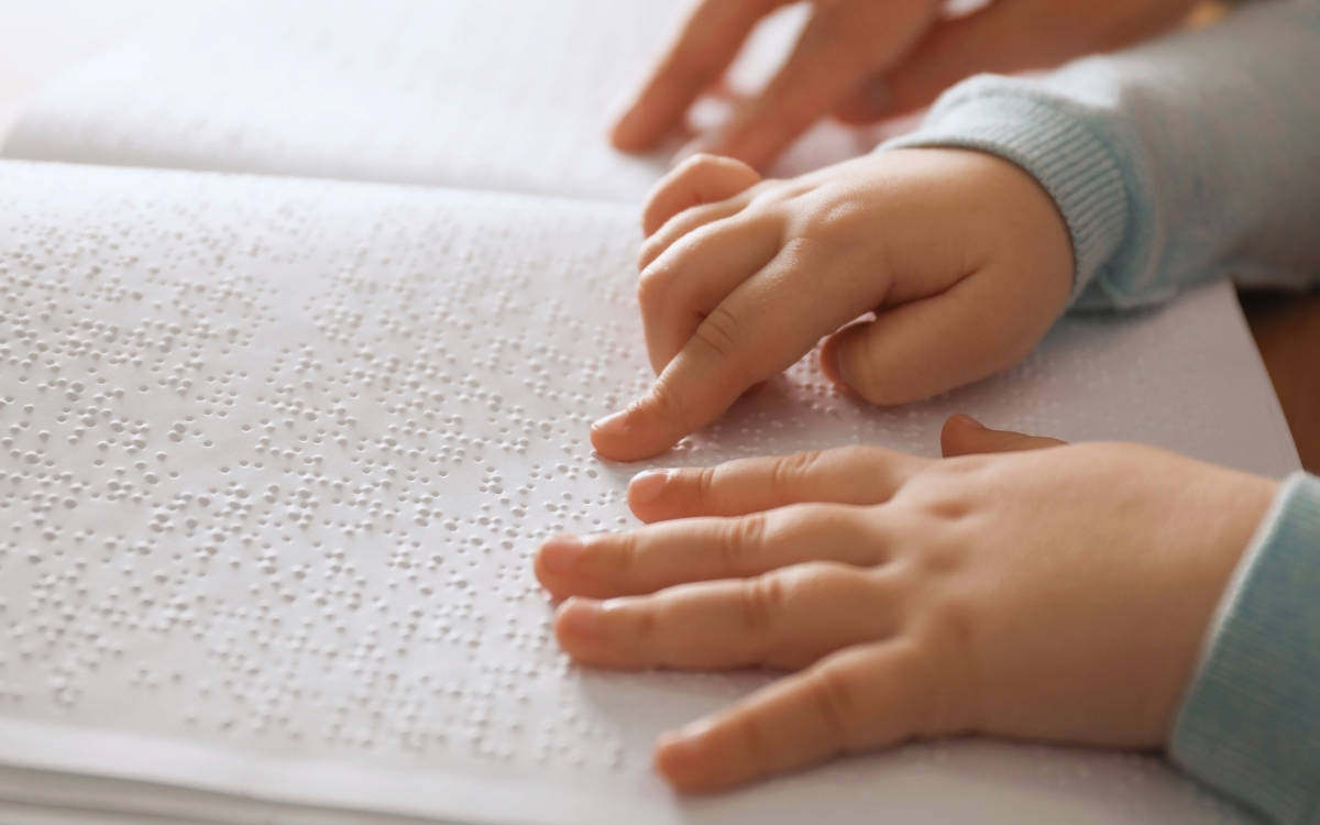 Braille Alfabesi ile kitap okuyan bir çocuğun temsili. Fotoğrafta bir kitap ve çocuğun parmakları var.