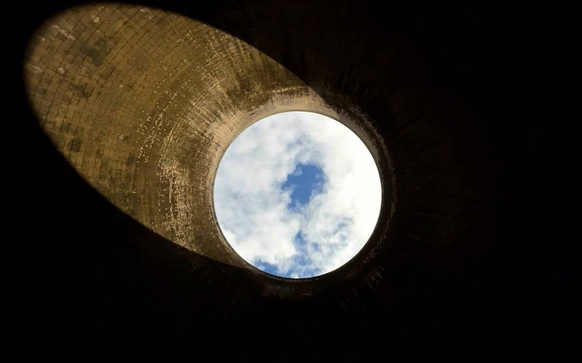 Görsel, bir kuyunun ya da silindirik bir yapının içinden yukarıya doğru çekilmiş bir fotoğrafı andırıyor. Silindirik yapının iç kısmı, taş ya da beton gibi sert bir yüzeyle kaplanmış görünüyor.