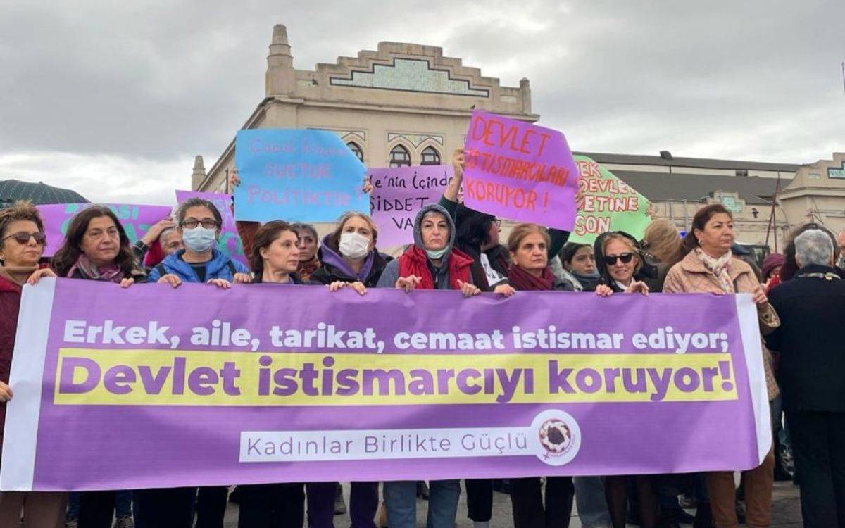 Fotoğraf, Türkiye'de kadın hakları ve toplumsal adalet konularında protesto gerçekleştiren bir grup kadını gösteriyor. Kadınlar ellerinde çeşitli pankartlar tutarak sloganlar ve mesajlar veriyor. Önde, büyük bir pankart dikkat çekiyor: "Erkek, aile, tarikat, cemaat istismar ediyor; devlet istismarcıyı koruyor!" Pankartın altında "Kadınlar Birlikte Güçlü" ifadesi yer alıyor, bu da katılımcıların dayanışma içinde olduklarını vurguluyor. Arkada ise, farklı renklerde pankartlar taşıyan kadınlar "Devlet istismarcıları koruyor!" gibi mesajlarla devletin bazı konulardaki tutumunu eleştiriyor. Göstericiler kararlı ve öfkeli görünüyor, yüz ifadeleri ve duruşlarıyla dikkat çekiyor. Etkinlik, toplumda istismara ve şiddete karşı bir farkındalık oluşturma çabasını yansıtıyor.