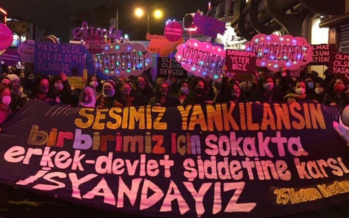 Görselde bir gece protestosunun görüntüsü yer almakta. Kadınlar, renkli ışıklarla süslenmiş pankartlar ve dövizlerle bir araya gelmiş. En öndeki büyük pankartta şu ifadeler yer alıyor:  "SESİMİZ YANKILANSIN, birbirimiz için sokakta, erkek-devlet şiddetine karşı İSYANDAYIZ"  Alt köşede küçük bir notta ise "25 Kasım Kadın" ifadesi görülebiliyor. Pankartın farklı renklerde ve büyük harflerle yazılmış olması mesajı vurguluyor.  Arka planda farklı dövizlerde şu tür ifadeler yer almakta:  "VİRÜS DEĞİL ERK-EK DEVLET ÖLDÜRÜR" "ŞİDDETİNE KARŞI" "DAYANIŞMA YETER BİZE" "OLMAZ OLSUN ŞİDDETİN YASASI" Eylem, muhtemelen 25 Kasım Kadına Yönelik Şiddete Karşı Uluslararası Mücadele Günü kapsamında gerçekleştirilmiş bir etkinliktir. Katılımcıların maskeli olması, pandemiye işaret edebilir. Bu tür bir protesto, kadın hakları ve dayanışma üzerine bir farkındalık oluşturma amacı taşır.