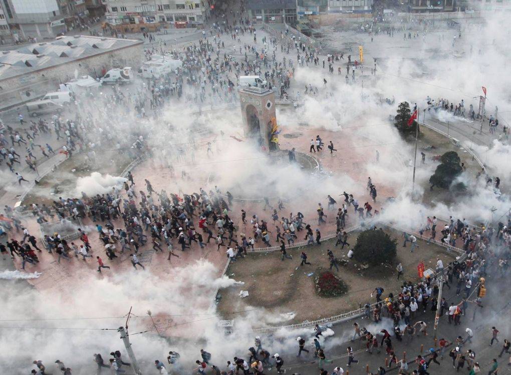 Bu fotoğraf, bir protesto veya toplumsal gösteri sırasında yoğun şekilde kullanılan biber gazı ve panik havasını yansıtan çarpıcı bir kareyi belgelemektedir. Görsel, kuşbakışı çekilmiş ve olayların merkezindeki meydanı —muhtemelen İstanbul Taksim Meydanı— tüm karmaşasıyla gözler önüne sermektedir.