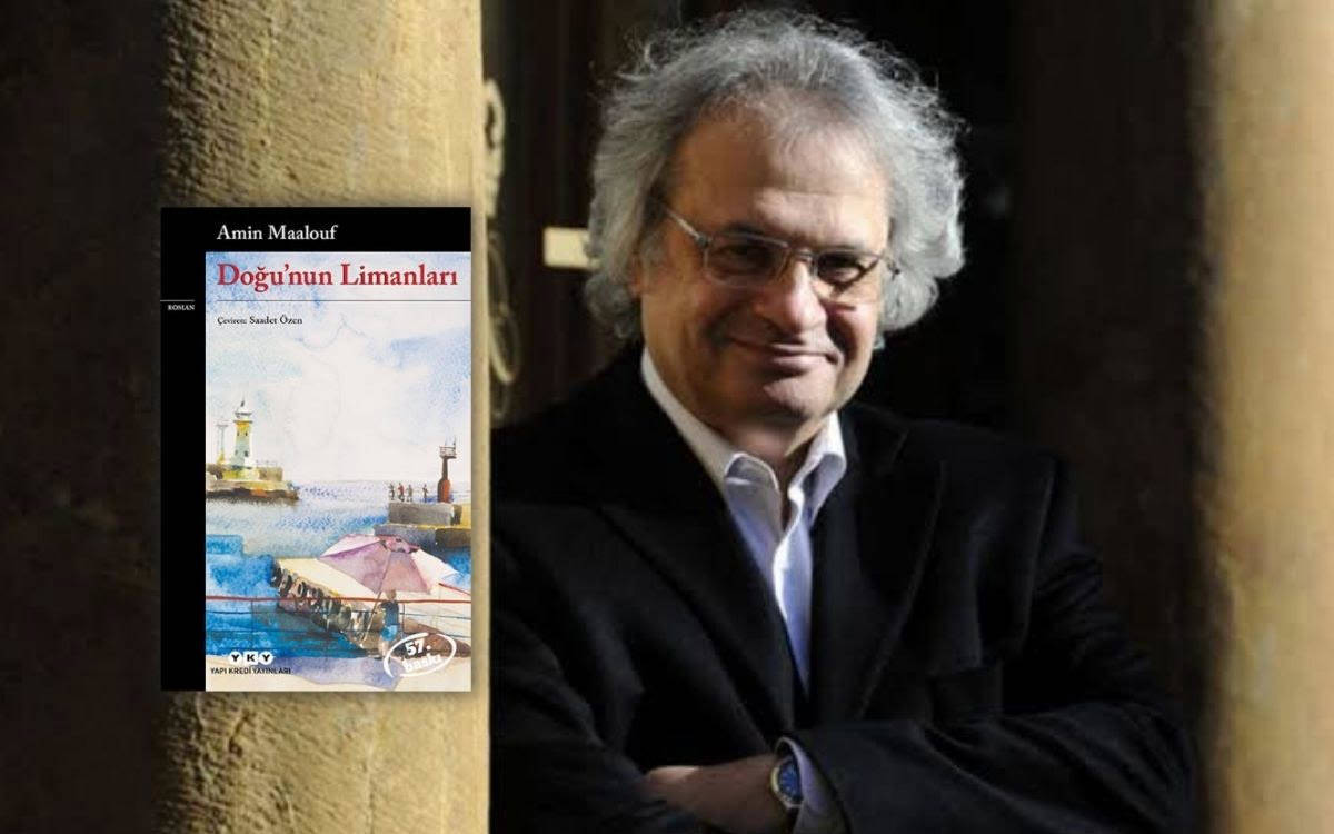 Bu görselde, Lübnan asıllı Fransız yazar Amin Maalouf yer alıyor. Yazar, koyu renkli bir ceket ve beyaz bir gömlek giymiş; gülümseyen ifadesi ve kollarını bağlamış rahat duruşuyla dikkat çekiyor. Gözlük takıyor ve saçları beyazlamış, dalgalı şekilde omuz hizasına dökülüyor. Arka plan loş ve taş dokulu bir yapının önünde çekilmiş gibi görünüyor, bu da ortama tarihî veya entelektüel bir hava katıyor.
