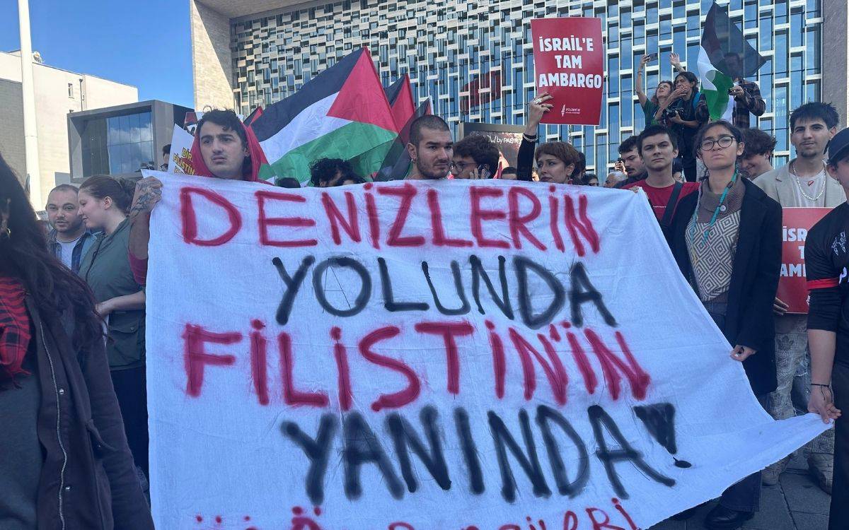 Fotoğrafta bir grup öğrenci açık havada toplanmış halde görülüyor. Kalabalığın önünde tutulan beyaz bir pankartta kırmızı ve siyah harflerle şu ifade yazıyor: “DENİZLERİN YOLUNDA FİLİSTİN’İN YANINDA! İTÜ ÖĞRENCİLERİ” (Bu betimle yapay zeka ile yapıldı)