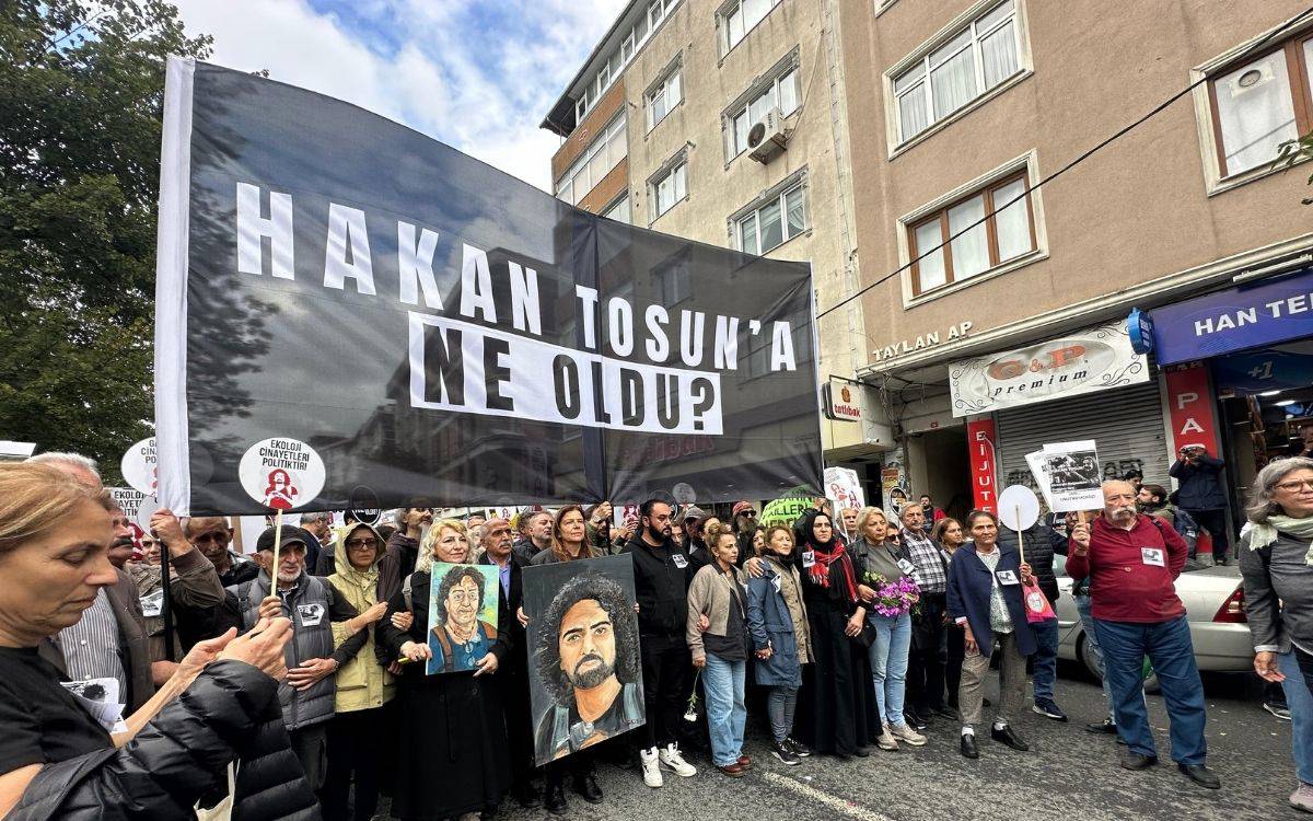 Fotoğrafta kalabalık bir grup, bir protesto ya da anma yürüyüşü sırasında bir araya gelmiş görünüyor. Ön sırada, büyük bir siyah pankart taşınıyor; pankartın üzerinde beyaz büyük harflerle “HAKAN TOSUN’A NE OLDU?” yazıyor.
