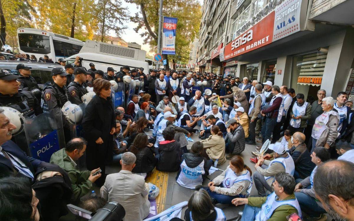 Fotoğrafta kalabalık bir protesto veya oturma eylemi görülüyor. Yüzlerce kişi bir caddede, kaldırım boyunca yere oturmuş durumda. Katılımcıların çoğu beyaz yelekler giymiş ve bazılarının üzerinde “KESK” yazısı okunabiliyor; bu da sendikal bir eylem olduğunu düşündürüyor.