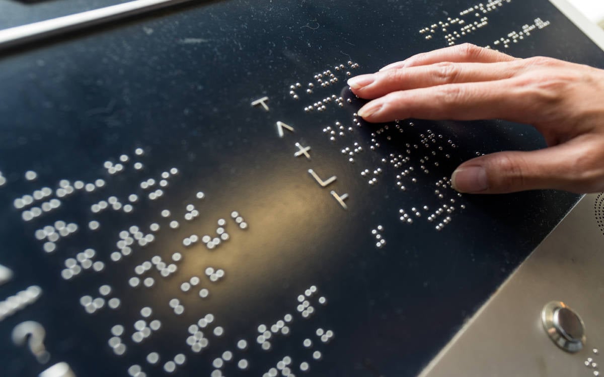 Hong Kong'daki bir parkta Braille alfabesi şeklindeki mesaj panosu ve mesajı okuyan kişi.